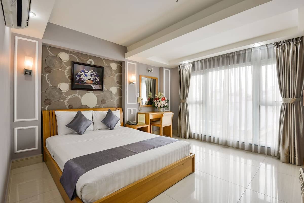A hotel room with a large bed, a desk, a mirror, and a view of the outdoors.