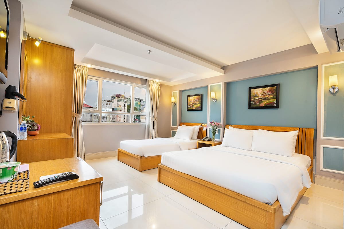 A hotel room with two beds, a desk with a remote control, a phone, and a window with a city view.