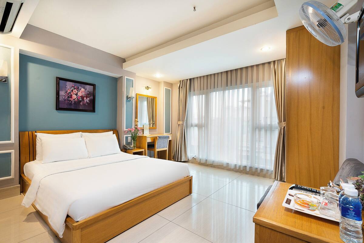 A hotel room with a large bed, a desk with a chair, a mirror, and a window with curtains.