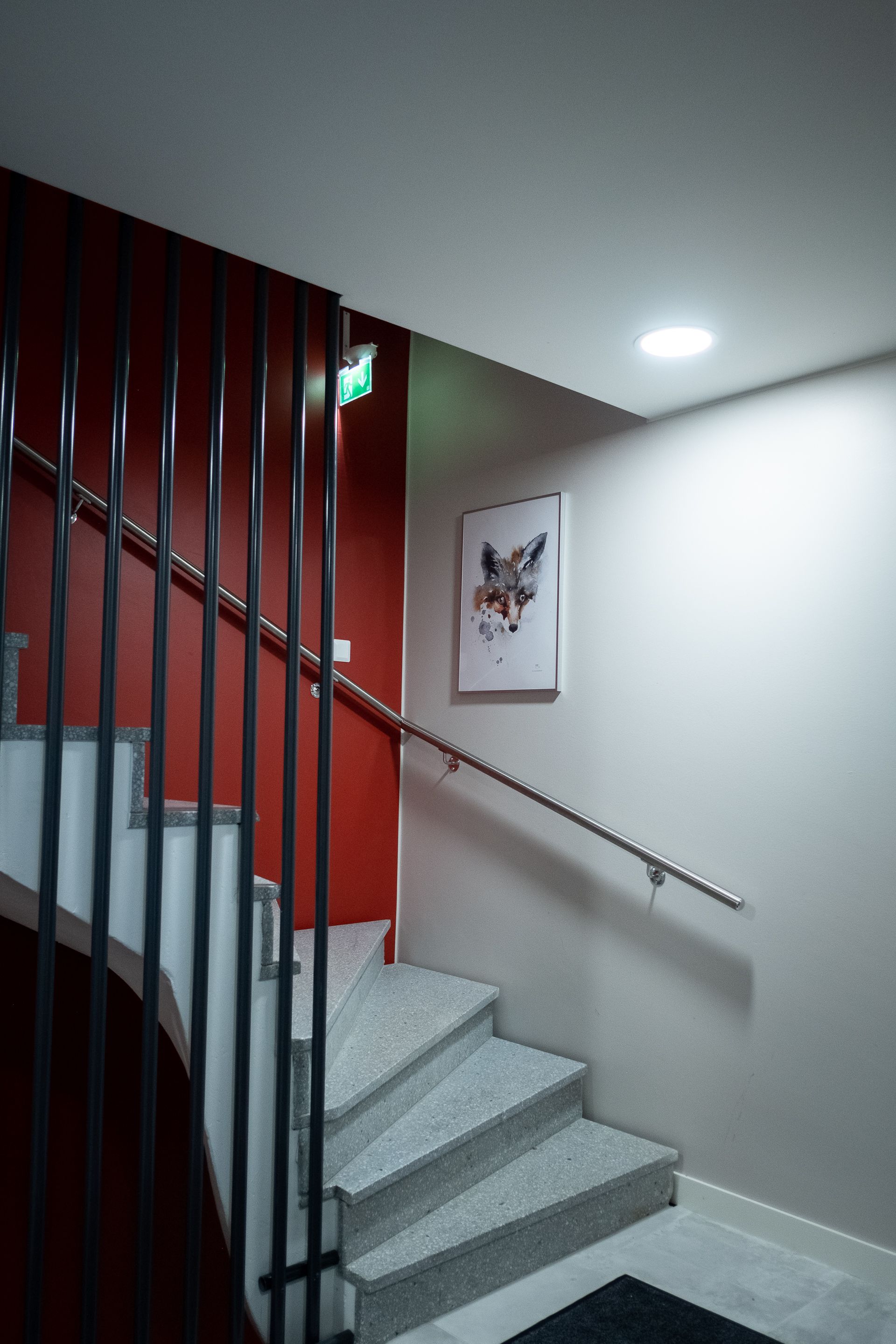 Een trap met een metalen leuning, een rode muur en een lijst met een kunstwerk erop.