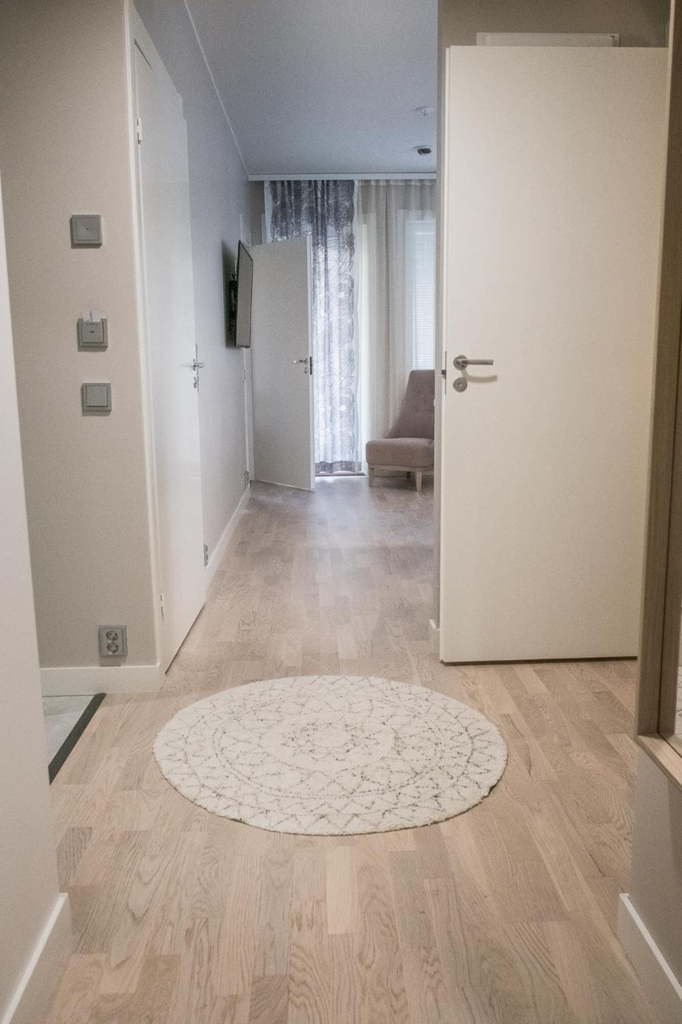 A hallway with a round rug, a door, and a chair in the background.