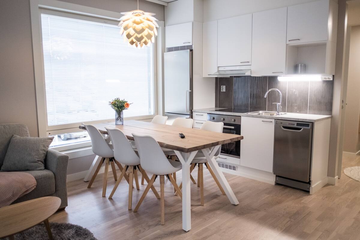 Una cocina moderna con armarios blancos, una mesa de comedor de madera y un lavavajillas empotrado.