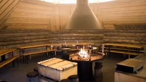 A rustic interior with wooden benches and tables arranged around a central fire pit. - Santasport Apartment Hotel (Rovaniemi)