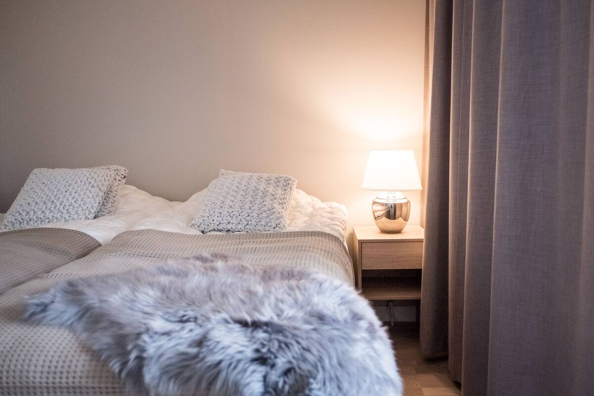 Una cama bien hecha con un almohadón mullido y una lámpara sobre la mesita de noche.