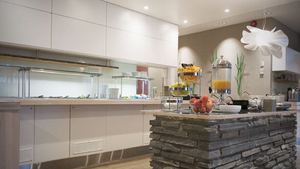 Una cocina moderna con una isla de piedra, estantes de vidrio para exhibición y diversos productos para el desayuno.