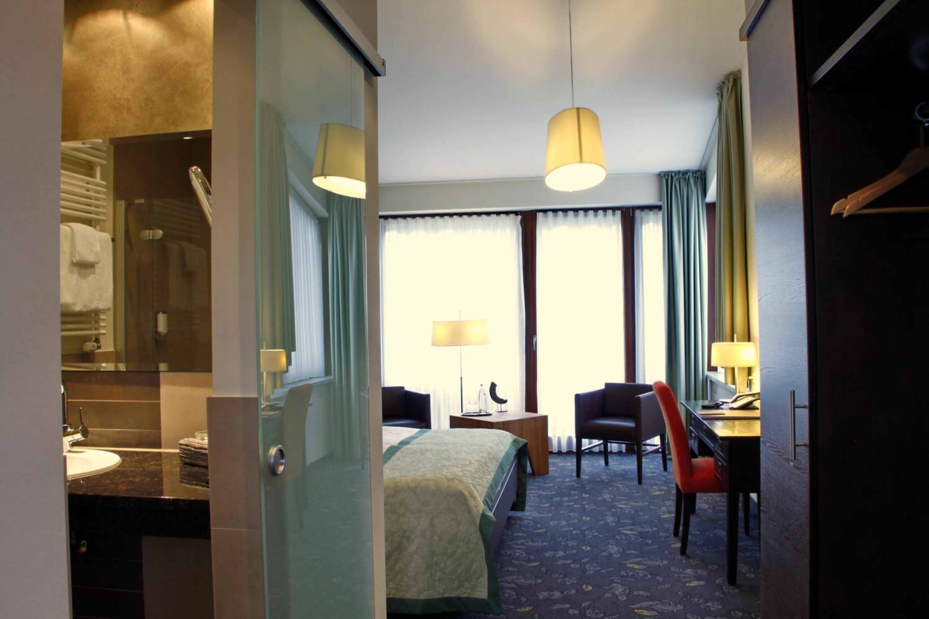 A hotel room with a bed, a desk, two chairs, a lamp, and a view of the outdoors.