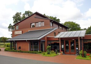 Um hotel com fachada de tijolos vermelhos, entrada coberta e uma placa indicando "Hotel Landhaus Pollmeyer".
