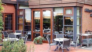 An outdoor seating area with tables and chairs, a brick building with large windows, and a sign that reads "The Lodge." - Hotel Landhaus Pollmeyer (Friesoythe)
