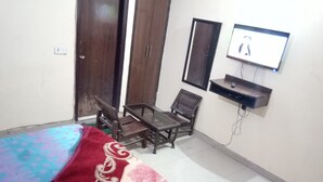 Une chambre à coucher comprenant un lit, une petite table, deux chaises, un téléviseur et une armoire.