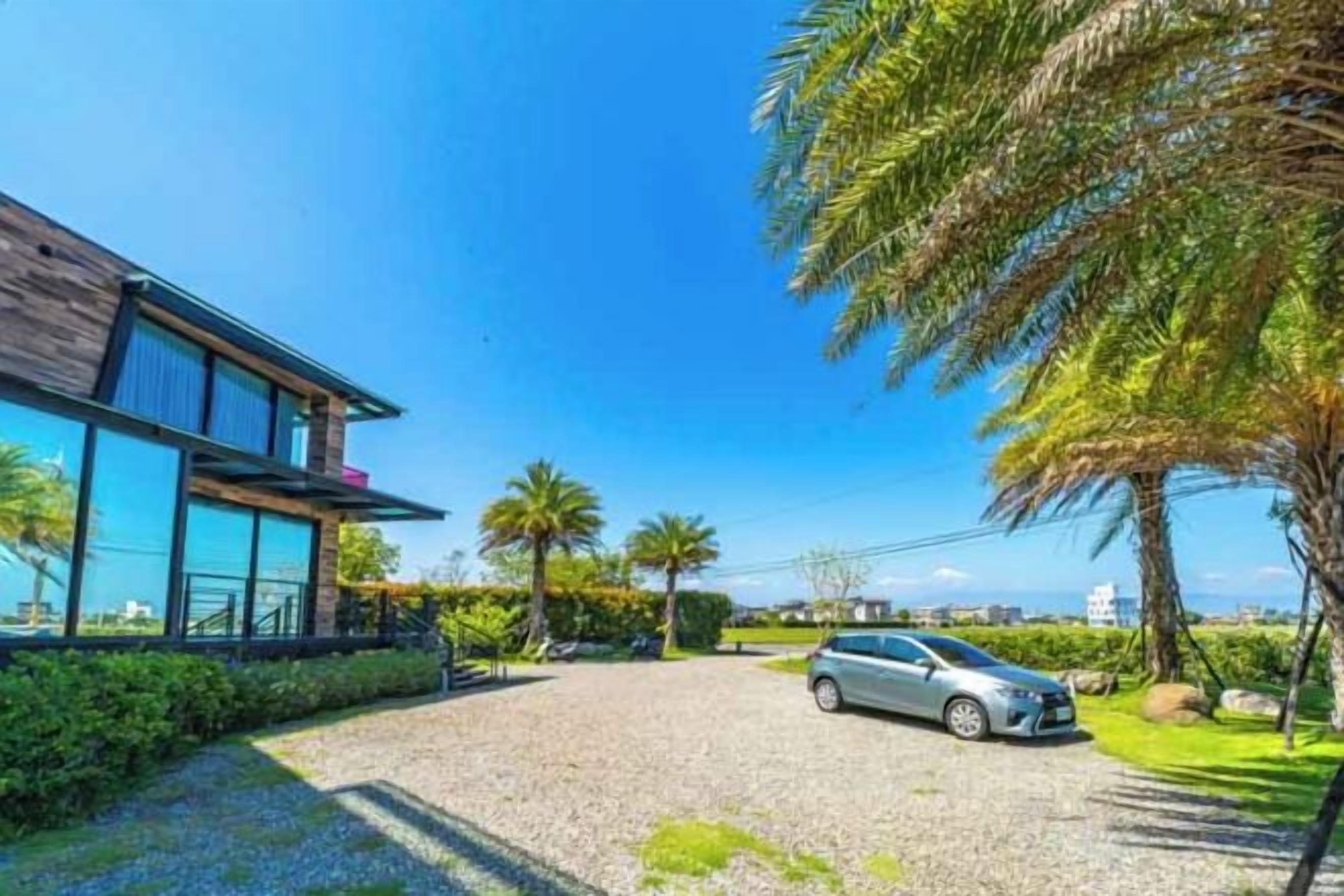 Una casa moderna con entrada de grava, un coche aparcado y palmeras.