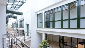 Um interior com vários níveis, teto de vidro, grades de metal e uma escadaria.