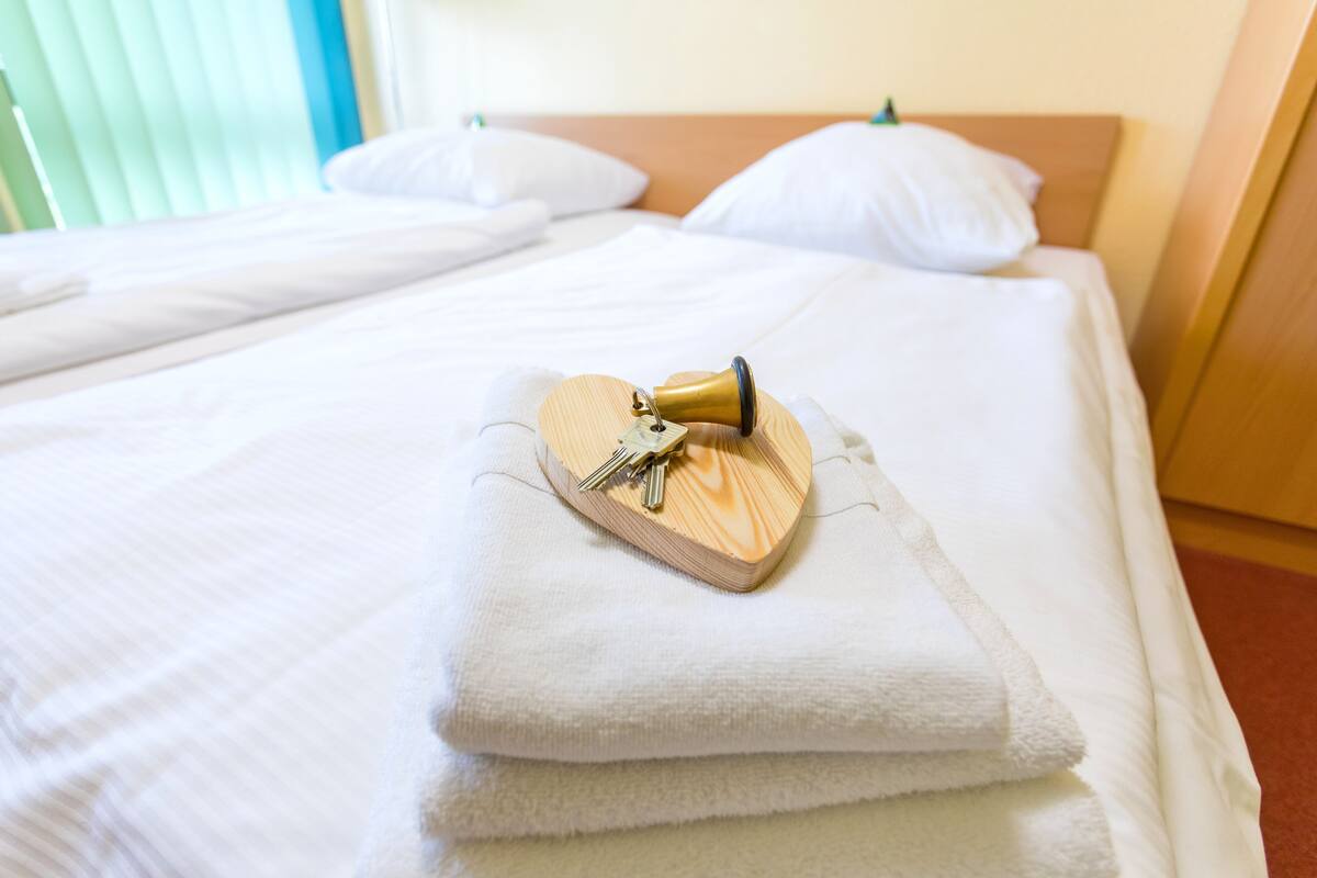 A neatly made bed with white linens, a heart-shaped wooden object with keys, and a wooden headboard.