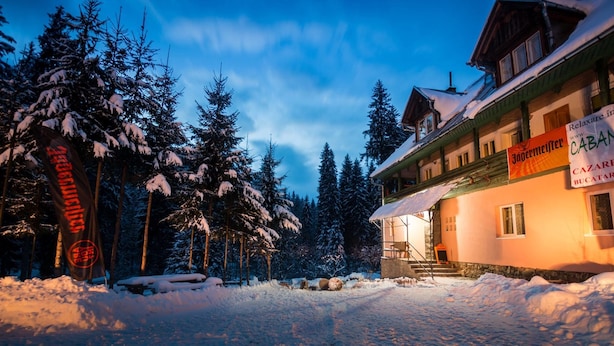 A snow-covered building with a wooden facade, surrounded by snow-laden trees. - Pensiunea Cabana Sestina (Lunca Bradului)