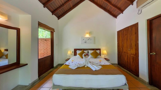 A bedroom with a wooden ceiling, a bed with white linens, two bedside lamps, and a wooden wardrobe. - Ehalagala Lake Resort (Sigiriya)