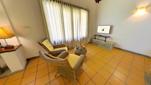 A living room with wicker furniture, a TV on a stand, and a lamp on a side table. - Ehalagala Lake Resort (Sigiriya)