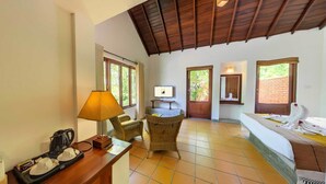 A hotel room with a wooden ceiling, a bed, a desk with a lamp, a chair, and a TV on a stand. - Ehalagala Lake Resort (Sigiriya)