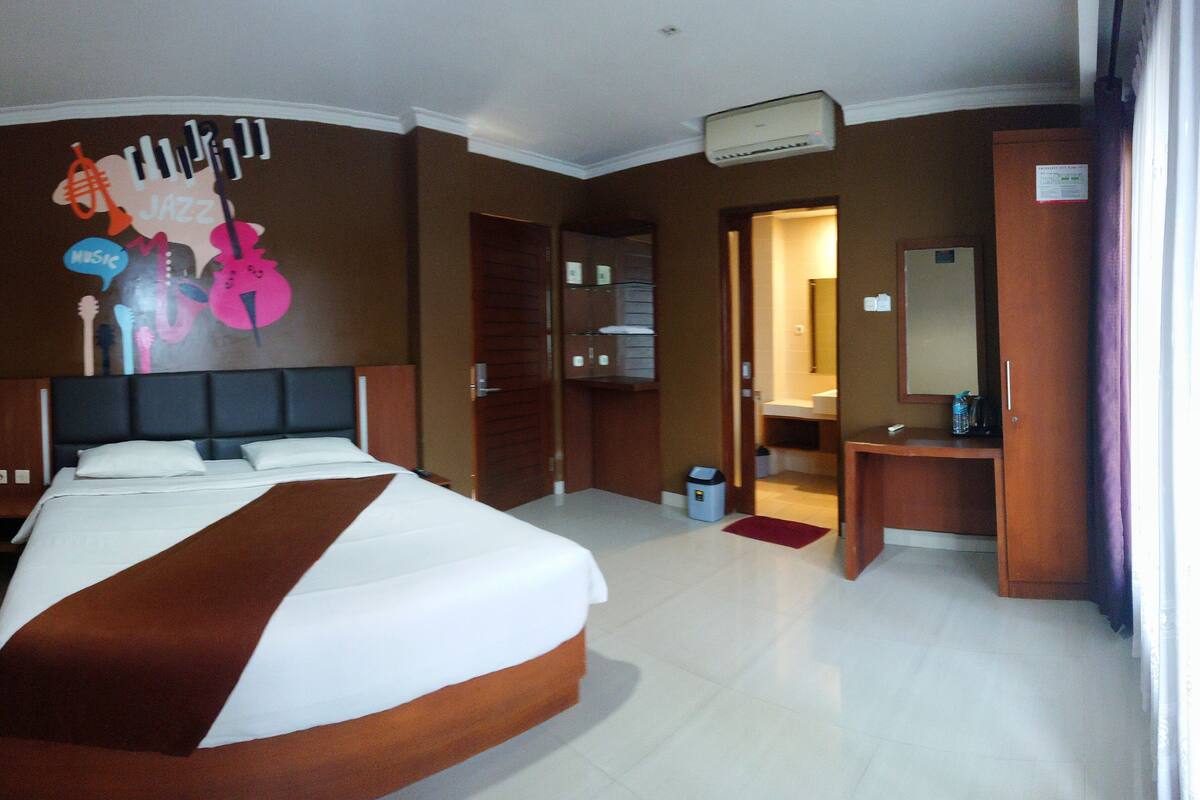 A hotel room with a large bed, a desk, a mirror, and a bathroom visible through an open door.