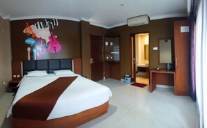 A hotel room with a large bed, a desk, a mirror, and a bathroom visible through an open door. - Votel Viure Hotel (Depok)