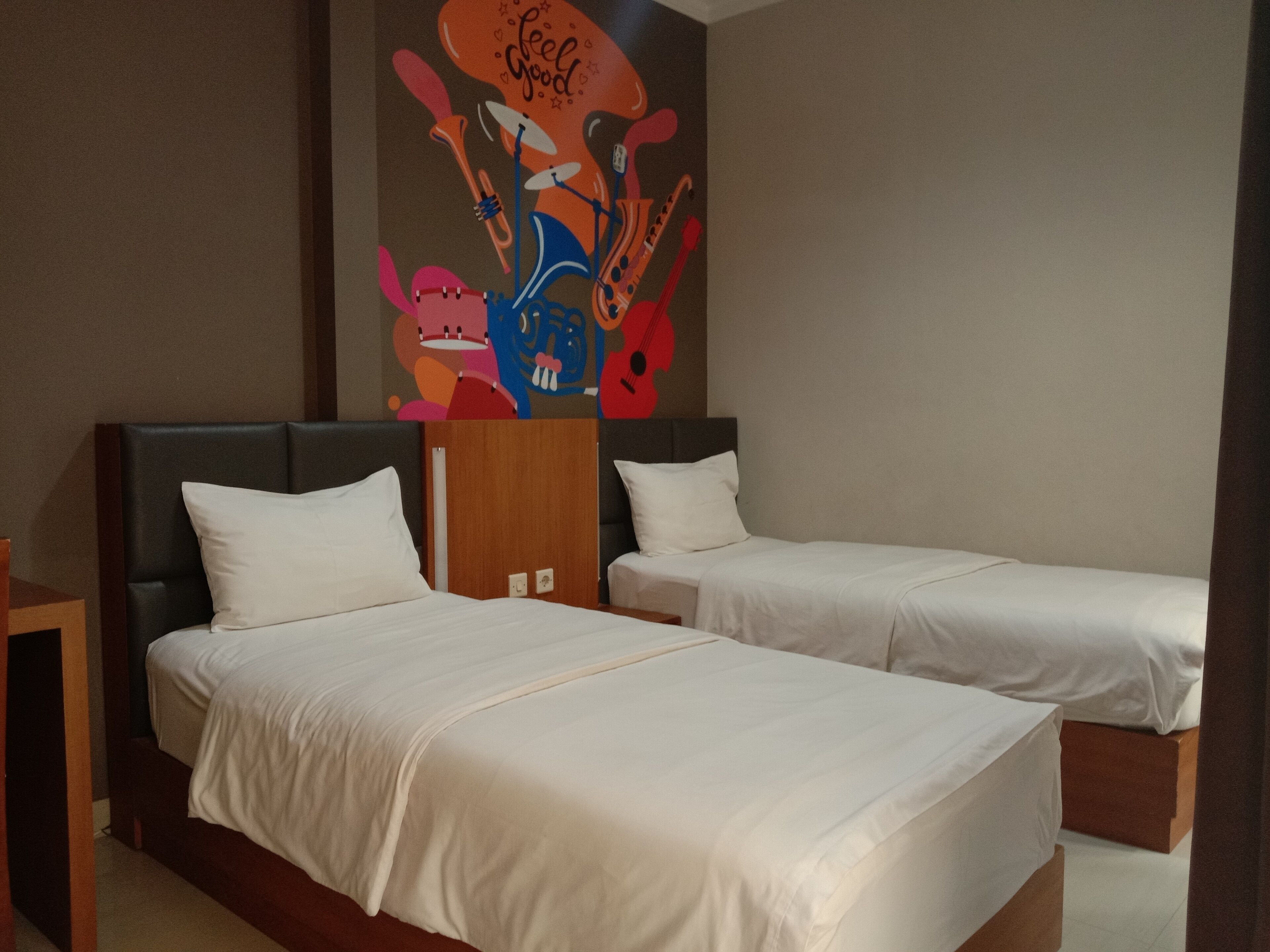 A hotel room with two single beds, a wooden headboard, and a colorful abstract painting on the wall.