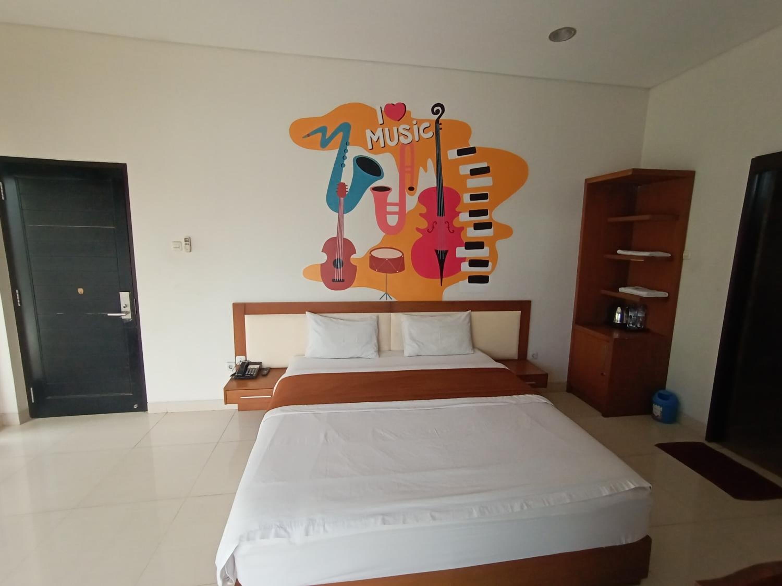 Una habitación de hotel con una cama, una mesita de noche, un mural en la pared con instrumentos musicales y un estante de madera.