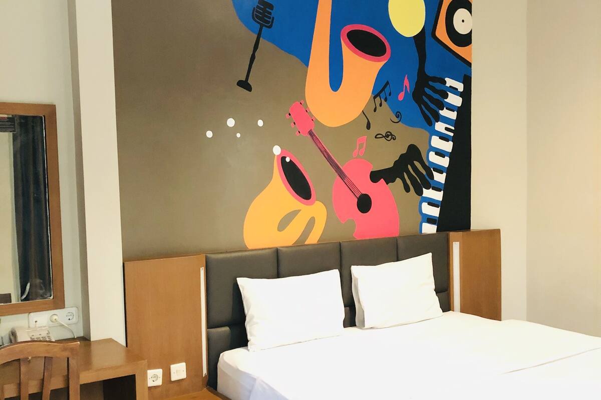 A hotel room with a bed, a desk, and a large wall mural depicting musical instruments and the word "Jazz".