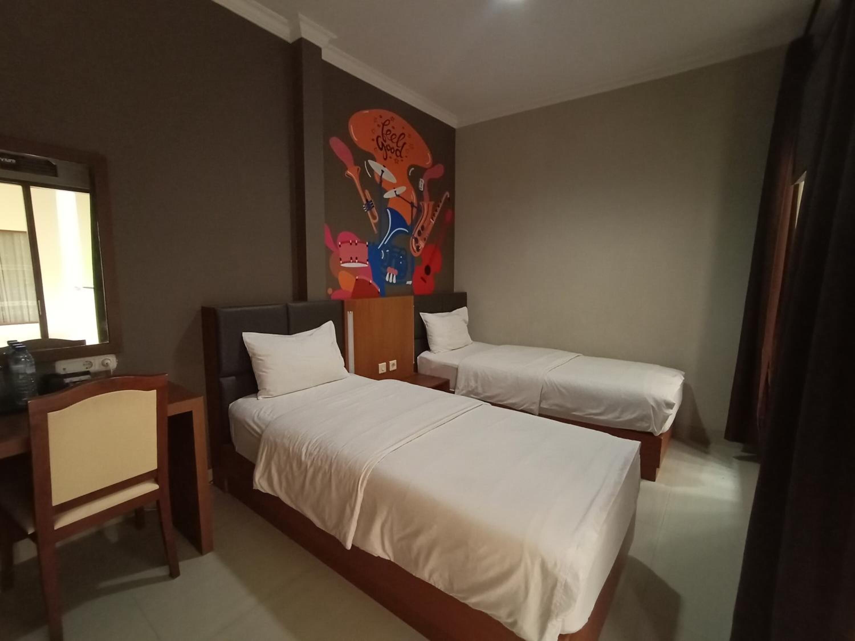 A hotel room with two single beds, a desk, and a chair.