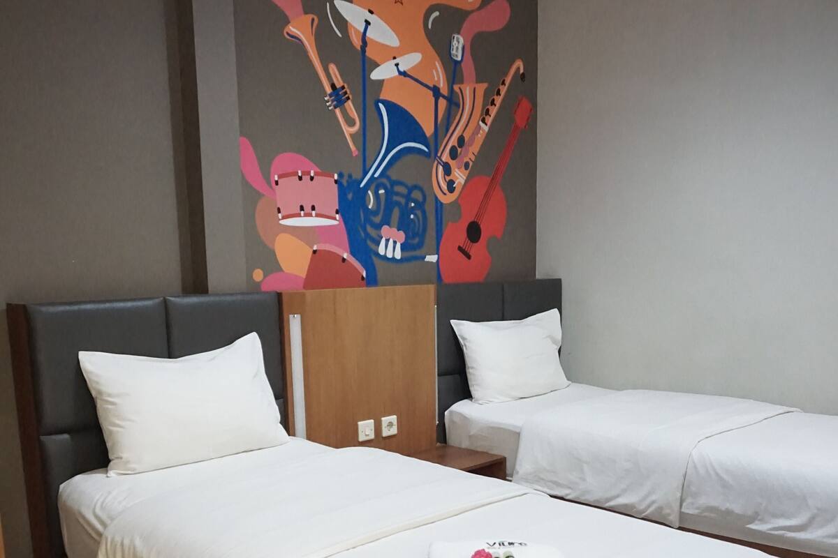 A hotel room with two beds, a mural on the wall, and a wooden headboard.