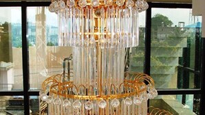 A multi-tiered chandelier with crystal decorations, hanging in front of a large window with a cityscape view. - Hotel Hilltop International (Port Blair)