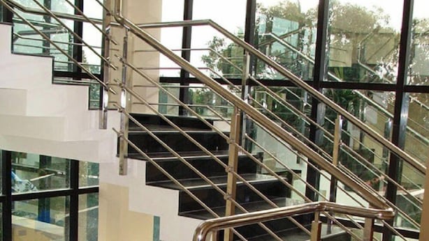 A modern interior with a glass and metal staircase, large windows, and a reflective floor. - Hotel Hilltop International (Port Blair)