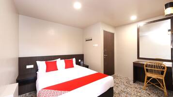 Cozy retreat with a large bed, nightstand, chair, and desk, set against a light-colored backdrop.