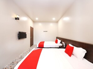 Een hotelkamer met twee bedden, een aan de muur bevestigde televisie en een klein nachtkastje met een fles.