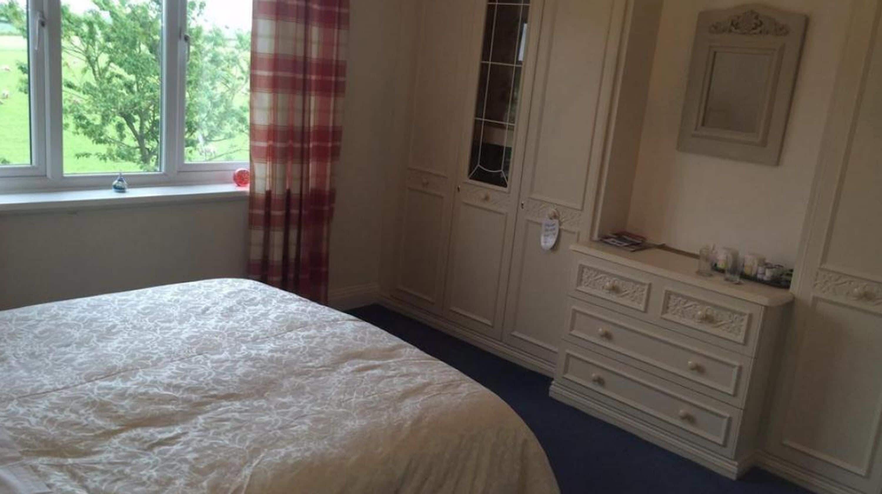 Ein Schlafzimmer mit Bett, Kommode, Spiegel und einem Fenster mit Vorhängen.
