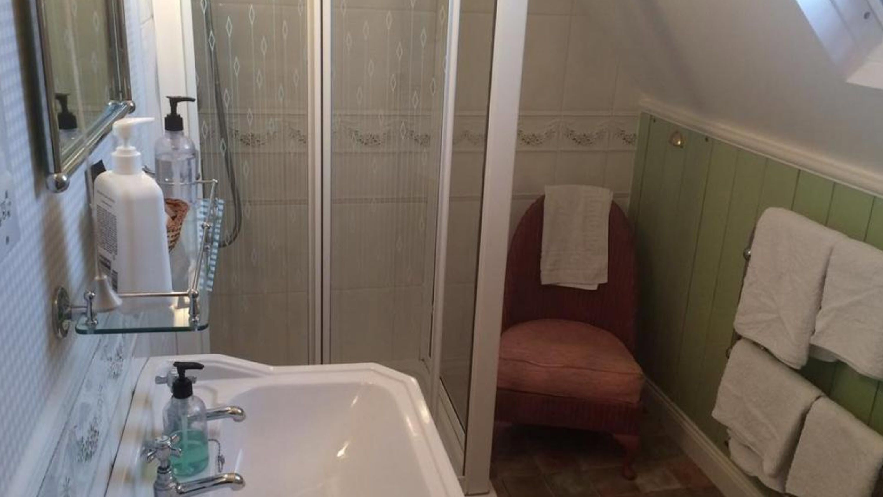 A bathroom with a shower, a sink with a soap dispenser, and a chair.