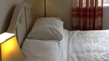 A bed with white bedding, a bedside lamp, and a window with red curtains.