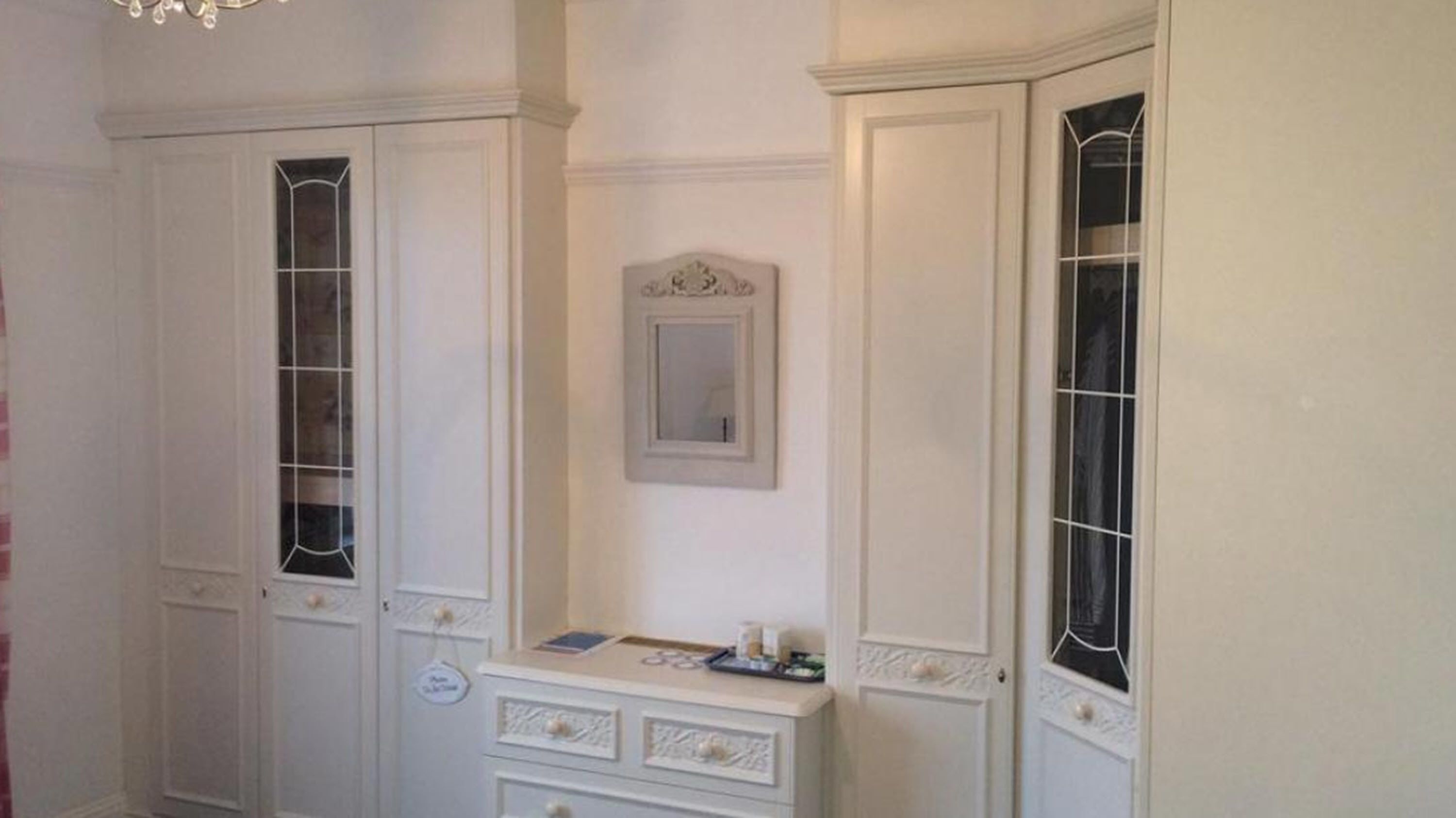 Una habitación con dos armarios blancos, una cómoda pequeña y un espejo en la pared.