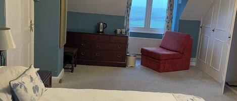 A bedroom with a bed, a red chair, a dresser, and a window with a view.