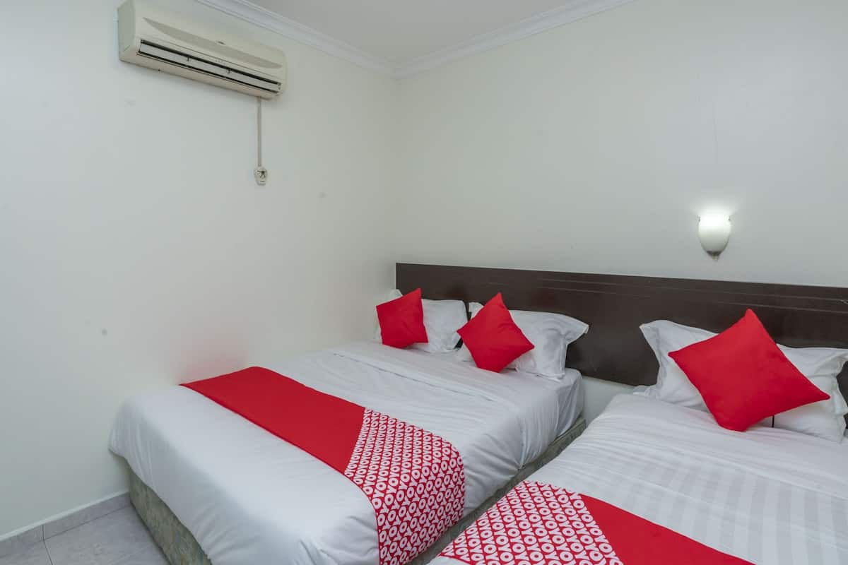 A hotel room with two beds, each with white bedding and red accents, a wall-mounted air conditioner, and a wall sconce.