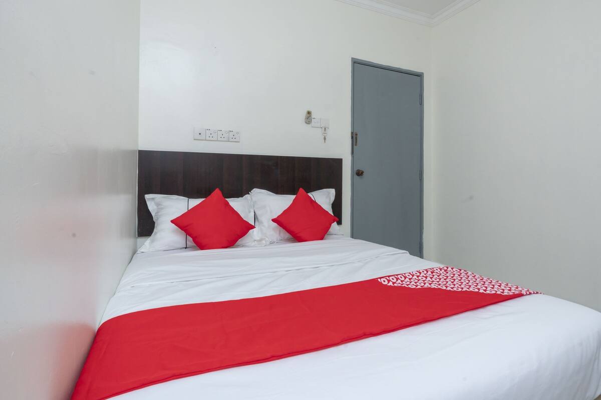 A neatly made bed with white and red bedding, a dark headboard, and a grey door.