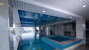 An indoor swimming pool with a blue-tiled edge, a ceiling with a cloud design, and a city view in the background. - The Twin B Palace Hotel & Apartments (Phnom Penh)