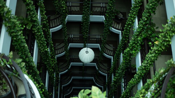 A multi-level atrium with a central hanging light fixture, surrounded by lush green vines. - The Twin B Palace Hotel & Apartments (Phnom Penh)