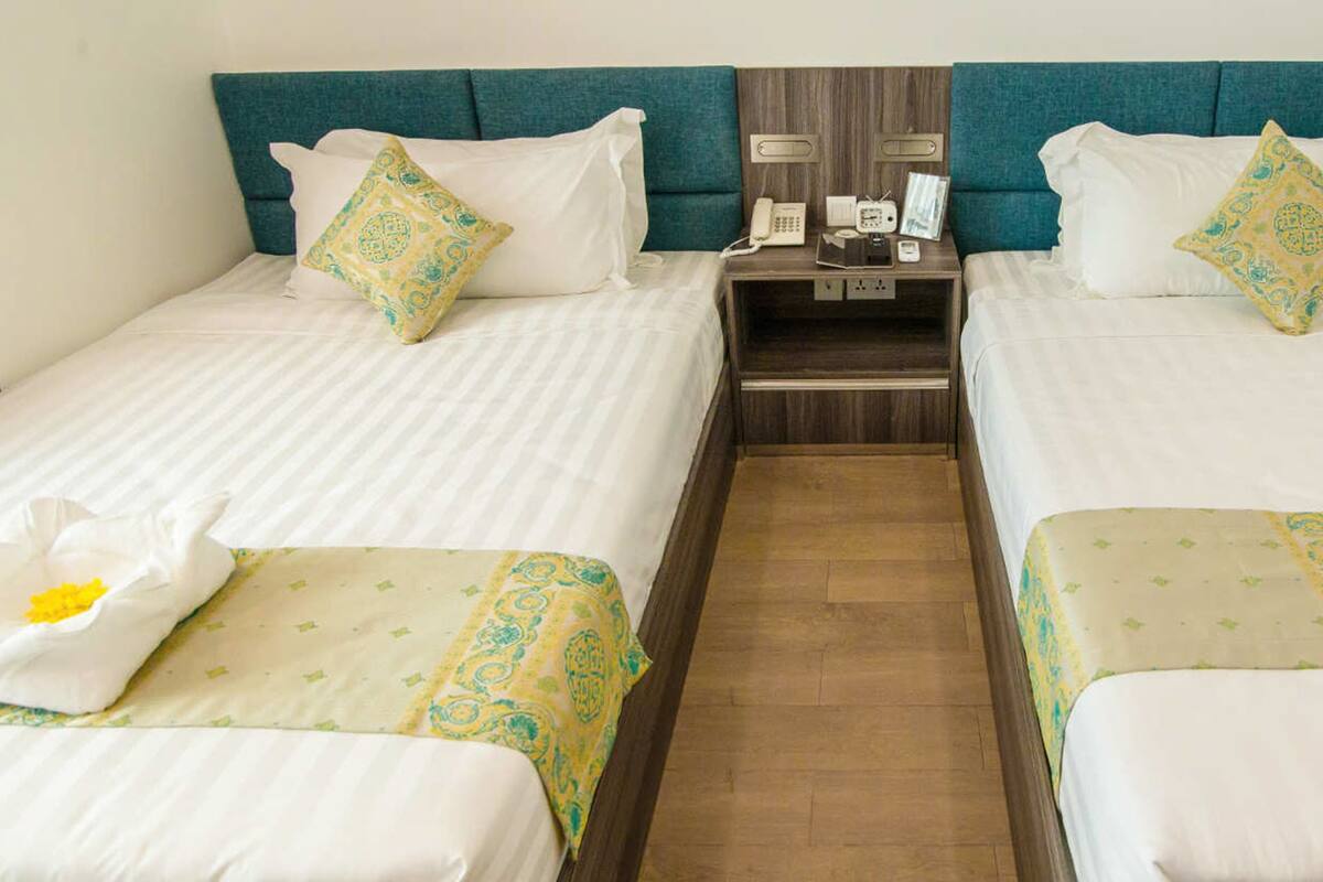 A hotel room with two single beds, each with a headboard, pillows, and a bedside table with a phone and a small lamp.