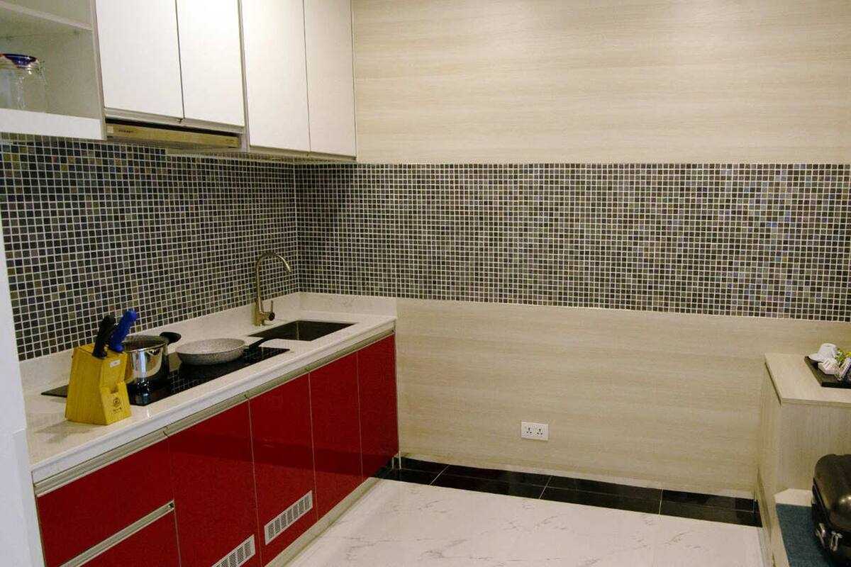 A compact kitchen with red cabinets, a black stove, and a tiled backsplash.