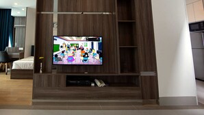 A modern hotel room with a large flat-screen TV mounted on a wooden wall, a bed, a desk, and a chair. - The Twin B Palace Hotel & Apartments (Phnom Penh)