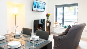 En moderne stue med spiseplads, et fladskærms-tv, pejs og et stort vindue.