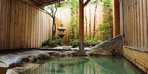 A traditional Japanese onsen with wooden walls, a stone lantern, and a rock-lined hot spring.