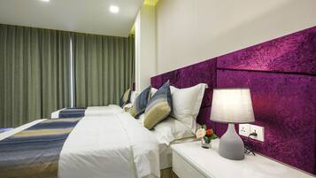 A hotel room with two beds, a purple headboard, a bedside table with a lamp, and a green curtain.