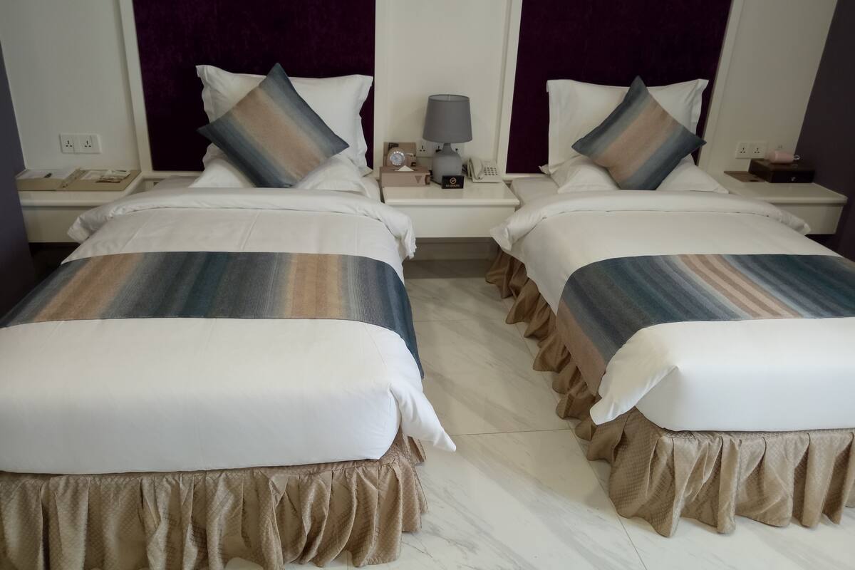 A hotel room with two beds, each with a striped bedspread, a nightstand with a lamp, and a wall-mounted phone.