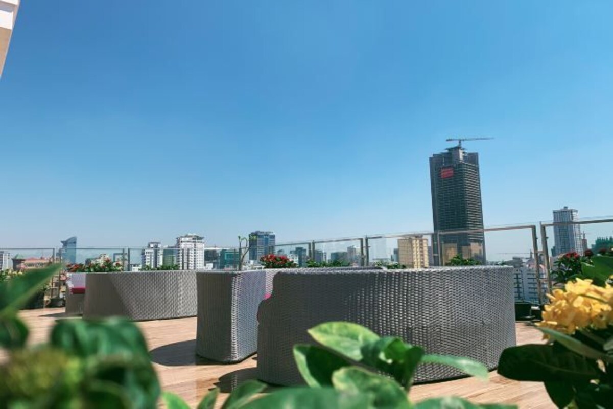 A rooftop terrace with wicker furniture and a city skyline in the background.
