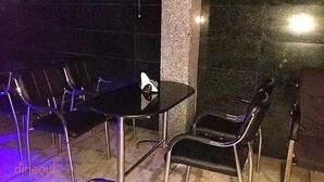 A small outdoor seating area with a round table and four chairs, surrounded by a low wall and a pillar. - Krishna International (Chennai)
