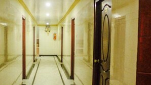 Un pasillo con suelo de mármol, puertas de madera y un extintor en la pared.